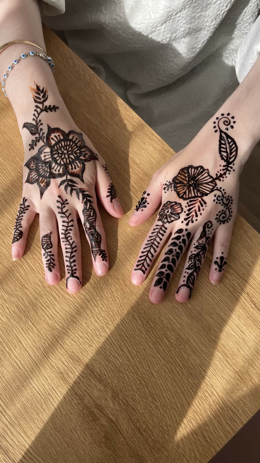 Black henna florals across both hands on a wood table in daylight
